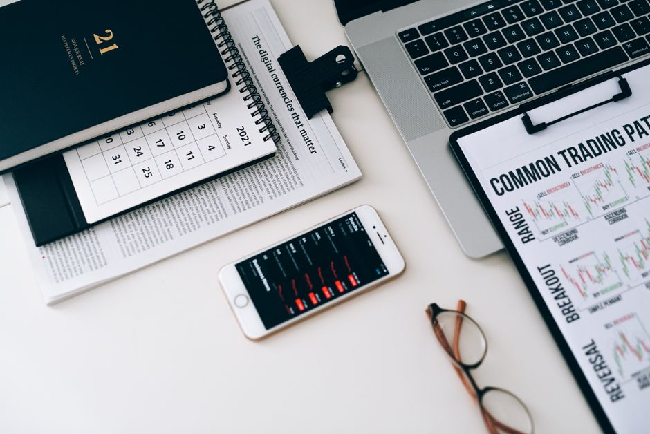 Home office desk featuring trading charts, smartphone, and laptop for financial analysis.