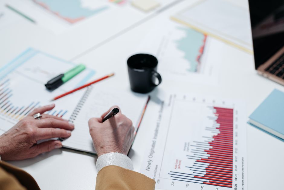 Close-up of hands writing in a notebook surrounded by business charts and documents.